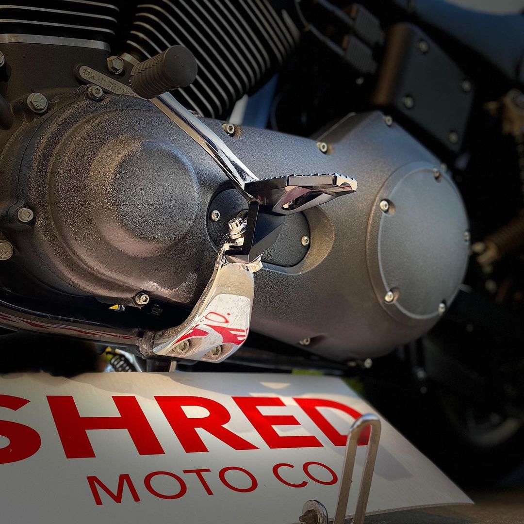 Shred footpeg assembly installed beside a Harley engine