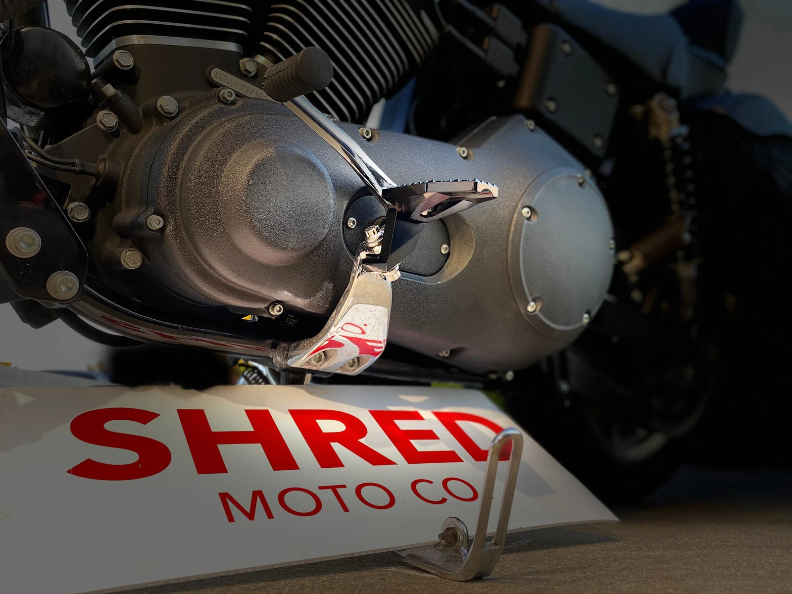 Machined Shred Pegs installed on a Harley, with the Shred Moto Co. sign below